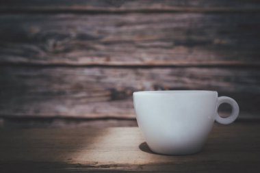 Tepesinden aşağı ışık saçan beyaz bir kahve fincanı ahşap bir tabağa ve ahşap bir zemin üzerine konur..