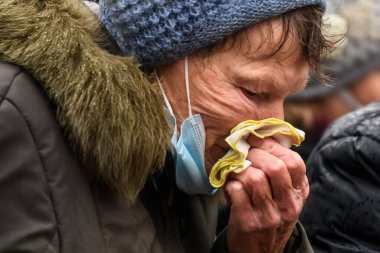 Koronavirüs Covid 'e karşı koruyucu maskeli yaşlı bir kadın Ukrayna, Kyiv' de sokakta burnunu siliyor. Ocak 2021