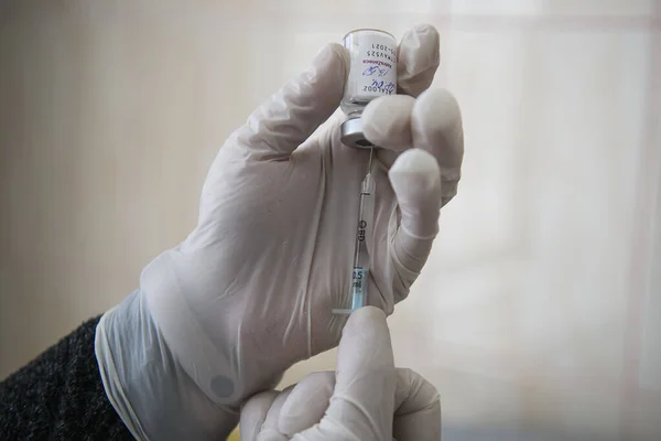 Руки медицинского работника в защитных перчатках удаляют дозу коронавируса AstraZeneca из флакона в больнице — стоковое фото