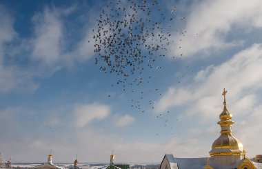 Altın kubbelerin üzerinde mavi gökyüzünde uçan güvercin sürüsü.