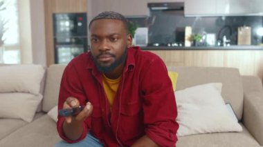 Yakışıklı, odaklanmış Afrikalı bir adam TV izlerken kanalı değiştirip kanepede oturup kilit altında tutulmak için en sevdiği dizileri arıyor. Eğlence. Sıradan insanlar..