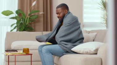 Hasta siyah Afrikalı bir adam battaniye giyip evde kalarak sıcak çayla ısınıyor. Virüs enfeksiyonunu tedavi ediyor. Kanepede otururken üşüten sağlıksız bir adam. Sağlık Hizmetleri.