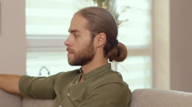 Kanepede rahatça oturan yakışıklı hippi, uzun saçlı genç adamın yüzü. Erkek portresi. Çekici insanlar. Evde kalma kavramı.