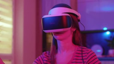 VR gözlüklü genç bir kadın, evdeki kanepede oturuyor. Neon ışıkta. Hareket eden eller. Teknoloji oyun yenilikçiliğini izole etti. Yavaş çekim