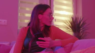 Gülümseyen kahverengi saçlı genç kadın geriye bakıyor. Randevu uygulamasında gülümseyen güzel bir kız. Pembe neon arka planda izole edilmiş, flört uygulamasında gezinen neşeli kızın portresi. Ev