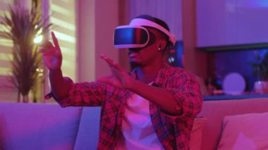 VR gözlük takan Afro-Amerikalı bir adam sanal simülasyon 3 boyutlu oyunlar yaşıyor ve evde artırılmış gerçekliği keşfediyor. Neon ışığı. Gece eğlencesi. Teknoloji konsepti.