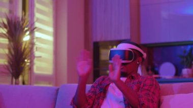 Komik Afrikalı Amerikalı mutlu adam sanal gerçeklik simülasyonu deneyleri yapıyor ve neon ışıklarla ev eğlencesi yapıyor. Gelecekteki teknoloji konsepti.