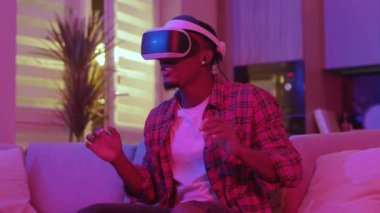 Sanal gerçeklik gözlüğü takan duygusal Afrikalı Amerikalı adam evde online oyunlar oynayan teknolojiyi algılayarak simülasyon oyunlarından zevk alıyor. Neon ışıkları.