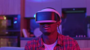 VR kulaklık takmış, ev eğlencesi için sanal oyun oynayan siyah bir adamın portresi. Futuristik oyunlar. Oyuncu. Neon aydınlatma. Komik aktivite.