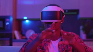 Evde oyun oynayan, VR gözlüklü genç bir adam sanal sanal sanal sanal oyunlar oynayarak eğleniyor. Neon ışığı. Modern yaşam tarzı.