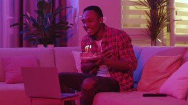 Mutlu Afro-Amerikan gündelik çocuğu çevrimiçi doğum günü partisini kutluyor pasta üzerine mum üflüyor ve neon ışıklı arkadaşlarıyla sohbet ediyor. Daire. - İnsanlar. Teknoloji.