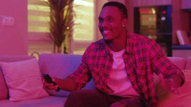 Heyecanlı Afro-Amerikan yakışıklı, coşkulu, coşkulu, coşkulu, coşkulu futbol fanatiği TV 'de maç müsabakaları izleyip neon ışıkları eşliğinde zaferi kutluyor..