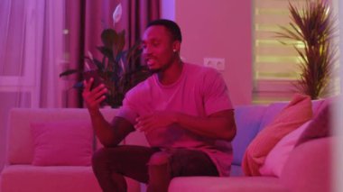 Neşeli Afro-Amerikan video blogcusu sosyal medya için çevrimiçi blog videosu yayınlıyor. Akıllı telefon sosyal medyasında arkadaşlarıyla uzaktan iletişim kuruyor. Neon ışıkları.