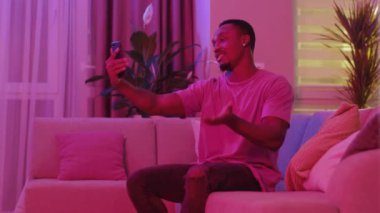 Sosyal Afro-Amerikalı sıradan bir adam akıllı telefondan ev videosu yayınlıyor ve yeni apartman ışıklarını gösteren webcam destekçilerine bakıyor. Teknoloji konsepti.
