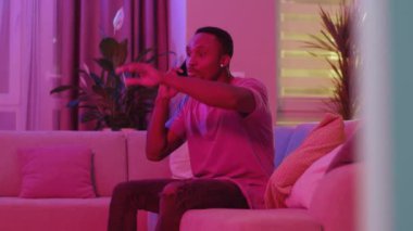 Kızgın Afro-Amerikalı sıradan bir adam telefonda kız arkadaşıyla tartışıyor oturma odasında hareketli hareketler yapıyor. Sohbet, arama. Neon aydınlatma. Ev dairesi.