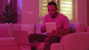 Çoklu görev. Neon ışıkları. Aynı anda birden fazla uzak iş yapan Afro-Amerikan serbest çalışanı bir kaç görevle uğraşırken sinirleniyor. İç mekan. Uzak iletişim.