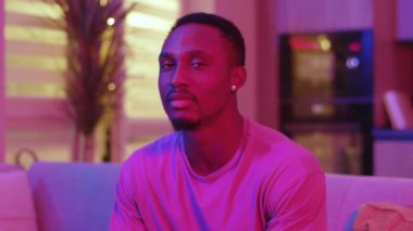 Çekici bir portre, kanepede oturmuş televizyon izlerken gülümseyen Afro-Amerikan sıradan bir genç. Neon aydınlatma. Tasasız yaşam tarzı.