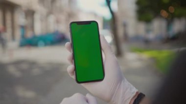 Akıllı telefon kullanarak Avrupalı genç adamın ellerini deri bilezik ile yakından çek. Kafkasyalı adam koruyucu eldiven takıyor sosyal medyada geziniyor, Coronavirus hakkında makaleler okuyor. Salgın