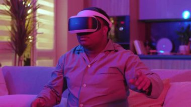 Neon ışığında gülümseyen melez ırk karşısında genç adam evdeki kanepede oturan sanal gerçeklik kulaklığını çıkarıyor. Eğlenceli oyundu. VR gözlükleri. Yavaş çekim
