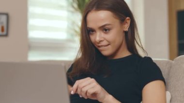 Kapalı kapılar ardında oturan yorgun kadın evdeki koltukta dizüstü bilgisayar kullanıyor. Stres genç yüz yorgunluğu çalışanı bir portre kanepesi. Yavaş çekim