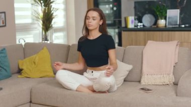 Kanepede oturmuş, evde gözleri kapalı meditasyon yapan genç bir kadın. Telefon meditasyonu yarıda kesiyor. Yavaş çekim