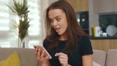 Merak ediyorum, genç bayan telefonda konuşurken koltukta otururken mutlu oluyor. Güneşli odada gülümsüyor. İnternet sosyal medya bağlantısı. Yavaş çekim