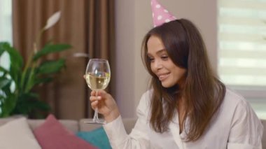 Doğum günü şapkası takan çekici genç bir bayan uzak arkadaşlarıyla internette video sohbeti yapıyor. Tatiller ve kendini izole etme. Sosyal mesafe. Karantina.