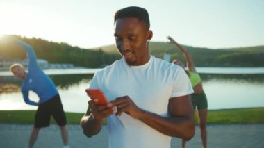 İki öğrenciyle sokakta egzersiz yapan mutlu bir Afrikalı eğitmenin görüntüsü. Genç, gülümseyen, atletik bir adam sosyal medyada blog yazıyor ve yararlı içerikler yayınlıyor. Sabah Vakti. Sağlıklı yaşam tarzının tanıtımı