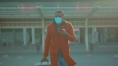 İndikten sonra havaalanından ayrılan, şık elbiseli, ciddi bir Afrikalı genç adam. Yüz maskeli, elinde telefonla internetteki popülaritesini toplayan bir adam. Koronavirüsü önlemek için yollar