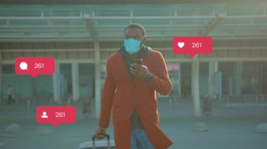 Koruyucu mavi maskeli genç bir Afrikalı bavuluyla havaalanında yürüyor, akıllı telefon kullanıyor, etrafa bakıyor. Son fotoğrafta sosyal ağlarda bir sürü beğeni ve yorum var. Kamusal alanlar, covid-19