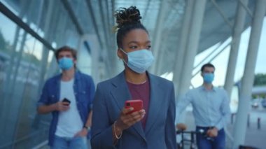 Geri döndükten sonra akıllı telefon kullanan tıbbi maskeli genç Afrikalı Amerikalı kadın. Salgın bir zamanda yolculuk yapmak. Yeni videolar ve fotoğraflar sosyal ağlarda birçok beğeni ve yorum topluyor. Açık havada.