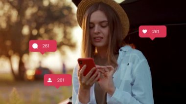 Tarz sahibi, beyaz saçlı, uzun kahverengi saçlı bir kızın yakın çekim görüntüleri. Beyaz tişörtlü ve şapkalı hoş hippi kadın arabanın yanında duruyor. Bulanık park geçmişi. Doğa. Açık havada. Dinlen. Gün batımı