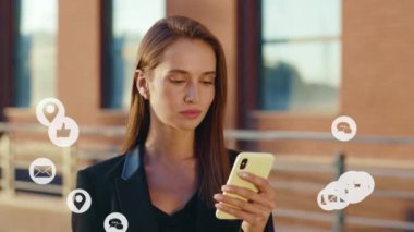 Çekici bir genç kadın telefon kullanır. Kamera tebessümüne bak. Sokakta dur. Vlog tutucu sosyal medya, uygulama simgeleri beyaz arayüzlü dijital animasyon. Yavaş çekim