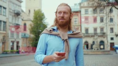 Gülümseyen sakallı adam şehir caddesinde telefon kullanıyor. Başarılı, kendine güvenen bir adam. Kullanıcı arayüzü - beğeni, takipçi, sosyal medya yorumları ile Vlogger etkili animasyon. Yavaş çekim