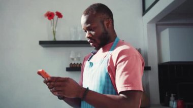 Afro-Amerikalı çekici bir adam yemek pişirirken internette geziniyor. Gülümseyerek mutlu ol. Kullanıcı arayüzü - beğeni, takipçi, sosyal medya yorumları ile Vlogger etkili animasyon. Yavaş