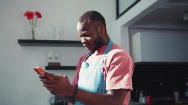 Afro-Amerikalı çekici bir adam yemek pişirirken internette geziniyor. Gülümsüyor. Kullanıcı arayüzü - beğeni, takipçi, sosyal medya yorumları ile Vlogger etkili animasyon. Yavaş çekim