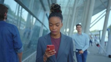 Genç, ciddi bir Afro-Amerikan kadın yürüyen portresi iş merkezinin yakınında telefon kullanıyor. Kullanıcı arayüzü - beğeni, takipçi, sosyal medya yorumları ile Vlogger etkili animasyon. Yavaş çekim