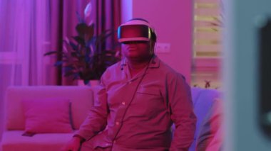 Neon ışığı. Sanal gerçeklik kulaklığı takan yakışıklı bir adam. Artırılmış Gerçeklik. Yaratıcı adam modern 3 boyutlu VR gözlükleri kullanarak bir şeye dokunuyor. Serbest çalışan öğrenci VR gözlüğü kullanıyor. Yakın çekim 4K
