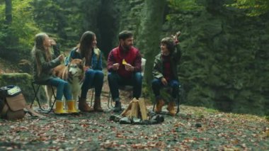 Sonbahar ormanlarında ateşin yanında oturup konuşan köpekli genç bir aile portresi. Çocuk gülen yaprak çevresi rahatlaması. Kapatın. Yavaş çekim