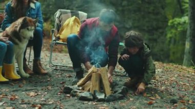 Sonbahar ormanlarında köpekli mutlu bir aile ateşin yanında oturup konuşuyor. Çocuk gülen yaprak çevresi rahatlaması. Kapatın. Yavaş çekim