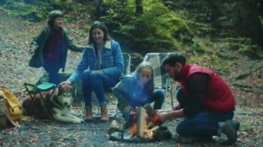 Aile sonbahar akşamı kamp ateşinin yanında oturur. Ebeveynleriyle birlikte çocuklar ormanda dinleniyorlar. Çocukluk ilişkisi kamp kuruyor. Kapatın. Yavaş çekim
