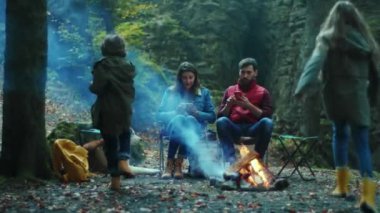 Mutlu aile sonbaharda kamp ateşinin yanında oturur. Çocukları ve aileleri ormanda. Çocukluk ilişkisi kamp kuruyor. Kapatın. Yavaş çekim