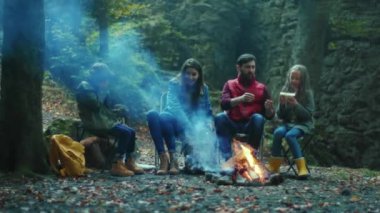 Mutlu aile, sonbahar ormanlarında kamp ateşinin yanında oturup yemek yer. Ebeveynleriyle birlikte çocuklar ormanda dinleniyorlar. Çocukluk ilişkisi kamp kuruyor. Kapatın. Yavaş çekim