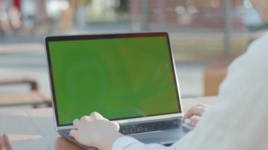 NEW YORK - 5 Eylül 2020: Beyaz tişörtlü genç bir kadının, yeşil ekranlı, daktiloyla gümüş dizüstü bilgisayarın başına oturması. İş kadını dışarıda çalışıyor, dokunmatik ped kullanıyor. Kafenin bulanık arkaplanı