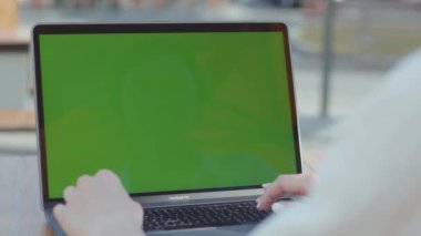 NEW YORK - 5 Eylül 2020: Kafenin yuvarlak ahşap masasında oturan ve yeşil ekranlı dizüstü bilgisayarla çalışan kadınların görüntüleri. Bilgisayarda yazan genç bir kadın. Güneşli bir gün. Yüzü olmadan. Kadın.