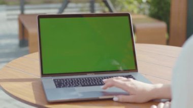 NEW YORK - 5 Eylül 2020: Laptop başında yeşil ekranlı beyaz bir kadının elleri. İş kadınının portatif bilgisayarla ahşap masada sohbet ederken yakın plan fotoğrafı.