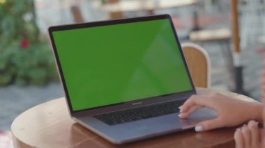 NEW YORK - 5 Eylül 2020: Gümüş dizüstü bilgisayarı kullanarak çiçek desenli elbiseli genç bir kadının yakın plan fotoğrafı. Halkla ilişkiler müdürü ahşap masada oturuyor ve elleriyle yeşil ekrana bakıyor.