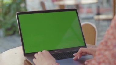 NEW YORK - 5 Eylül 2020: Kafede ahşap masada oturan ve dizüstü bilgisayar kullanan çiçek desenli elbiseli genç bir kadın omzu. Güzel manikürlü, klavyede yazı yazan kadın elleri. Renkli bulanık arkaplan