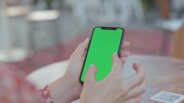 NEW YORK - 5 Eylül 2020: Yeşil ekranlı akıllı telefonu tutan, dokunaklı ekranı olan, yakınlaştıran izole bir kadının elleri. Cep telefonu kullanan genç bir kadının görüntüsü. Açık havada. Bulanık arkaplan