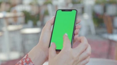 NEW YORK - 5 Eylül 2020: Elinde yeşil ekranlı akıllı telefon tutan, parmaklarıyla işaret eden, kafede öğle yemeği arasında zumlayan genç kadın. Dışarıda cep telefonu kullanan bir iş kadınının elleri. Kamu alanı